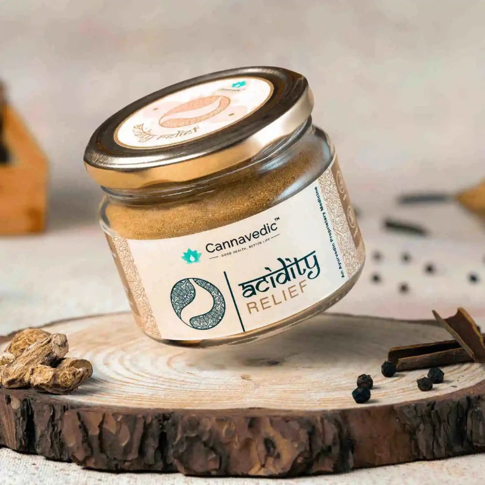 Jar of Cannavedic Acidity Relief powder on a circular wooden slab with dried roots, peppercorns, and cinnamon.