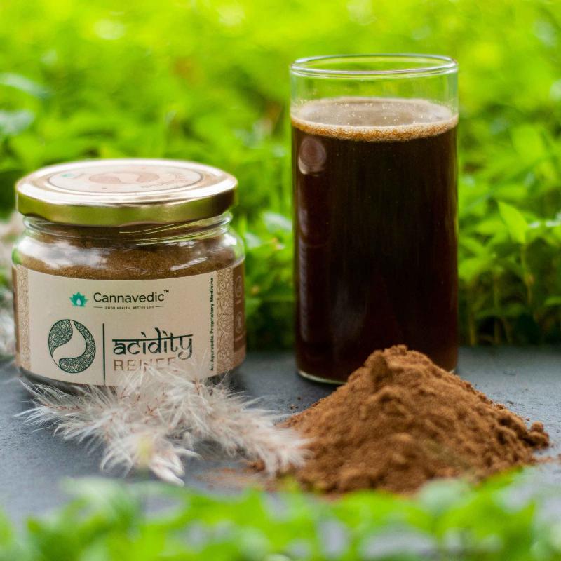 A jar labeled "Cannavedic acidity RELIEF" and a small pile of brown powder on a dark surface with green foliage in the background.
