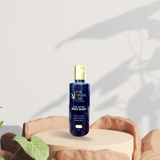 Bottle of "The Divine CBD" body wash on a round pedestal with plant shadows in the background.