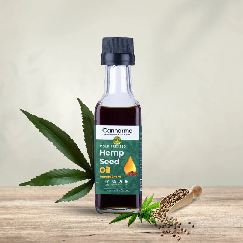 Bottle of cold-pressed hemp seed oil with hemp leaves and seeds on a wooden surface.