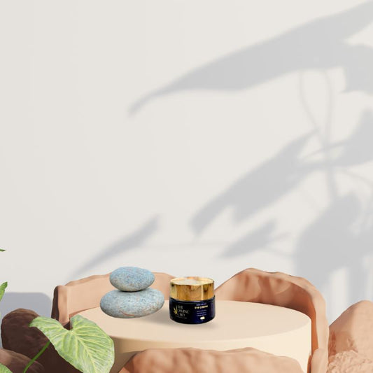 Pedestal table with two pebbles and a jar, surrounded by rocks and leaf in the corner.