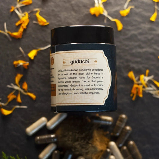 Jar labeled "Guduchi" with scattered yellow flower petals and capsules in white and dark grey colors.