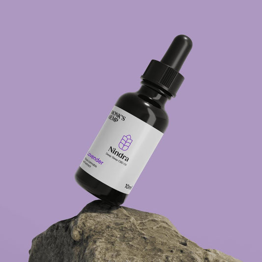 A dark glass bottle with a dropper cap labeled "Nindra Deep Sleep CBD Oil" balanced on a rock.