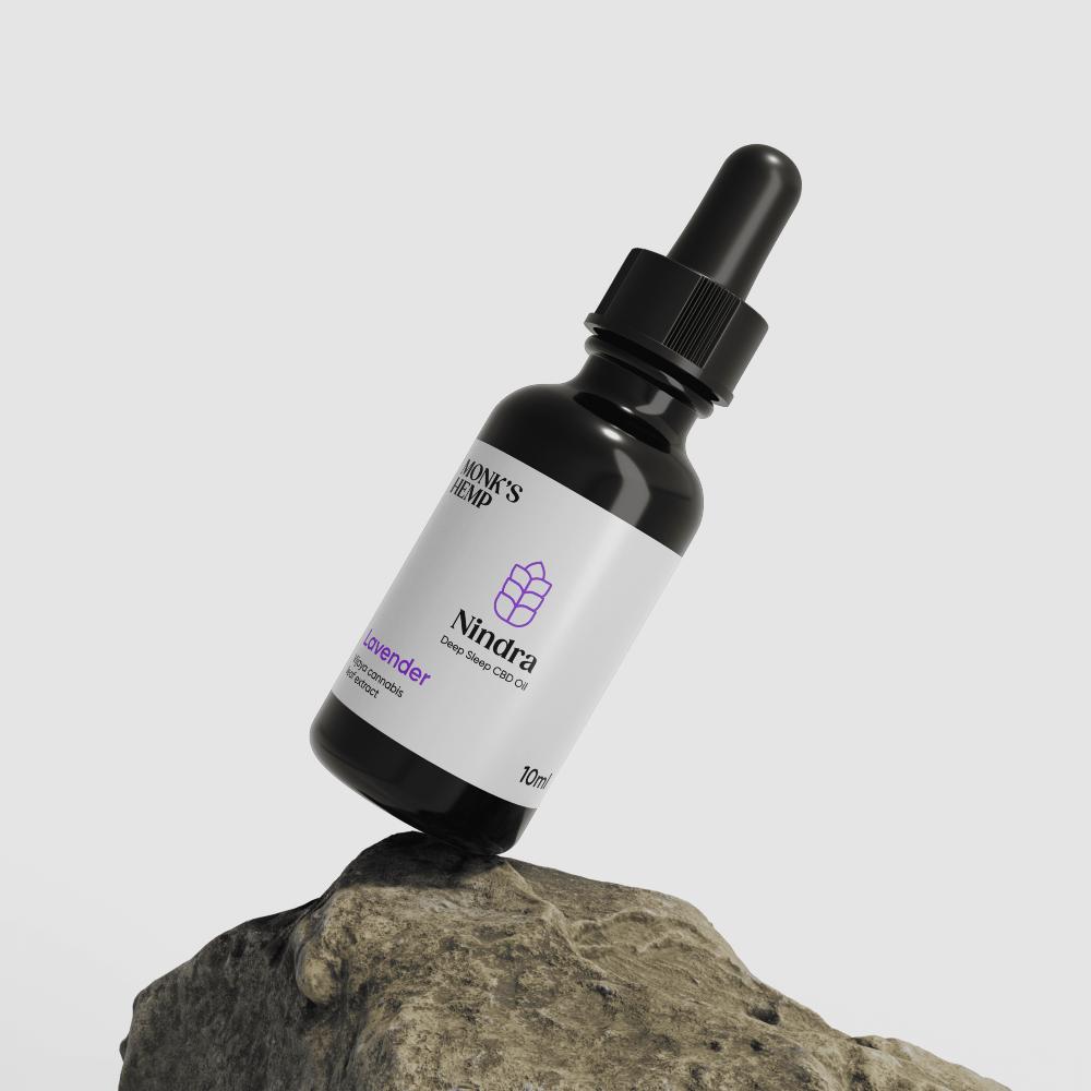 A small bottle of deep sleep CBD oil with a dropper cap, labeled "MONK'S HEMP Nindra" and posed on a gray rock.