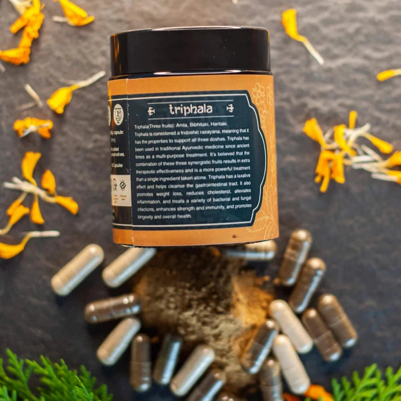 A container of Triphala with scattered yellow flower petals and capsules around it.