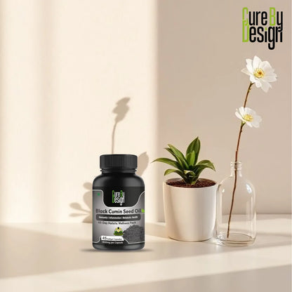 Bottle of 'Pure By Design' black cumin seed oil on a surface with a plant and vase in the background.