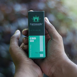 Close-up of hands holding a box of Cannavedic CBD Oil with the label "0% THC, 100% CBD" and "Icy Mint".