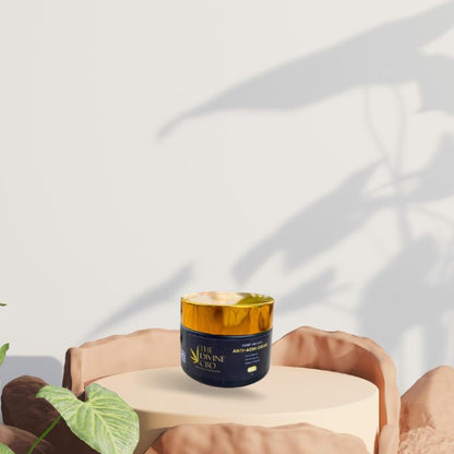  A small jar with a gold lid and dark blue body on a light beige pedestal, surrounded by rocks and a green leaf, with leaf shadows in the background.

