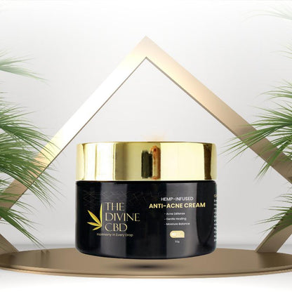 Black container of The Divine CBD Anti-Acne Cream with a gold lid against a white background with green plants.

