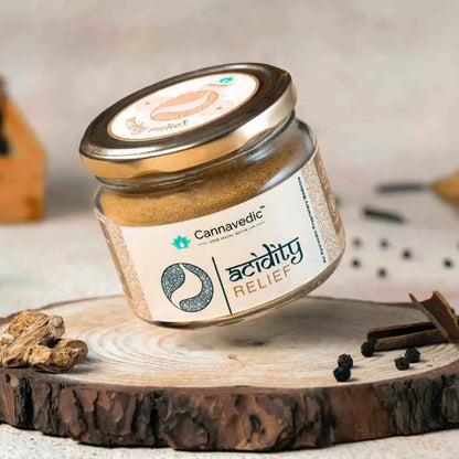 Jar of Cannavedic Acidity Relief powder on a circular wooden slab with dried roots, peppercorns, and cinnamon.