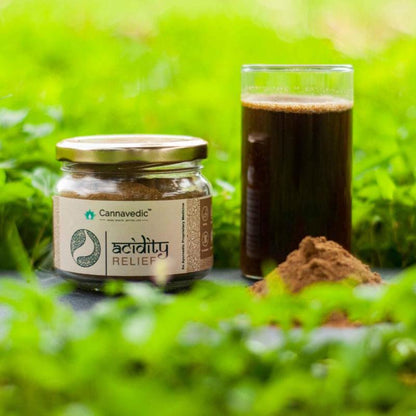 Jar of "Cannavedic Acidity Relief" powder next to a glass of dark liquid and a small mound of the powder in a green, leafy background.