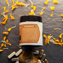 Load image into Gallery viewer, Black container of Ashwagandha with capsules and powder surrounded by marigold petals and green foliage.
