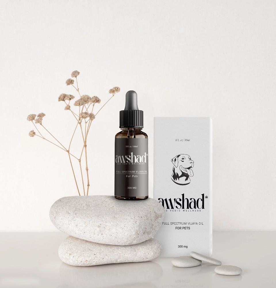 A dropper bottle labeled 'awshad Full Spectrum Vijaya Oil for Pets' beside its packaging and decorative stones.