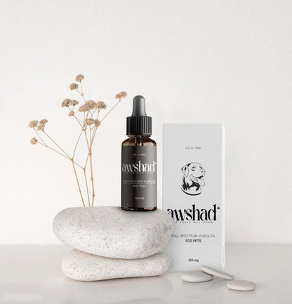 A dropper bottle labeled 'awshad Full Spectrum Vijaya Oil for Pets' beside its packaging and decorative stones.