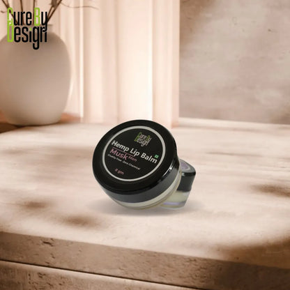 Hemp lip balm container on a wooden surface with 'Cure By Design' branding.