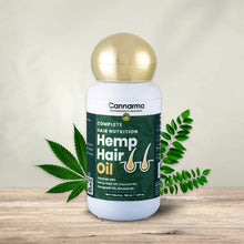 Load image into Gallery viewer, A light-colored background highlights a wooden display featuring a hemp hair oil bottle with a gold lid and leafy green accents.
