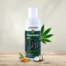 Load image into Gallery viewer, Bottle of Cannaarma Psoriasis oil with a cannabis leaf, coconut, and turmeric root on a wooden surface.
