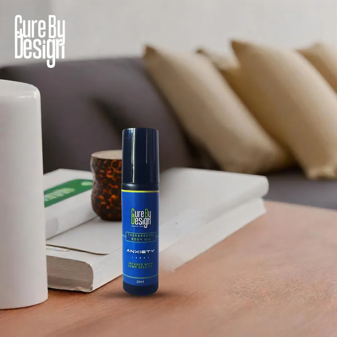 Blue bottle labelled 'Cure By Design Anxiety therapeutic body oil' on a wooden surface with a blurred background