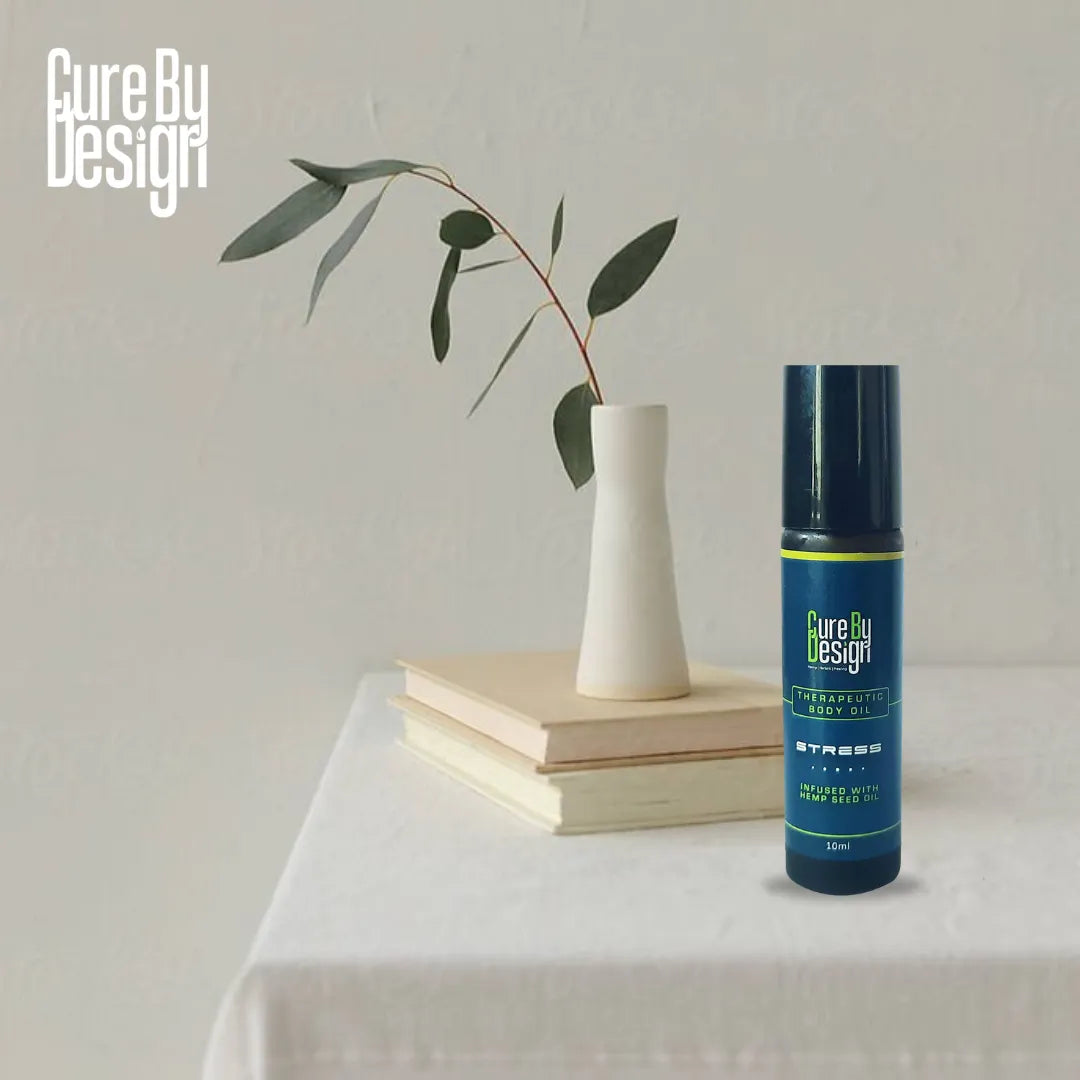 Bottle of Cure By Design Therapeutic Body Oil for Stress, on a table with a vase and books in the background