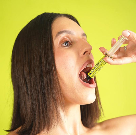 Person using a syringe with yellow label to administer a dark liquid, medical cannabis extract. Lime green background.