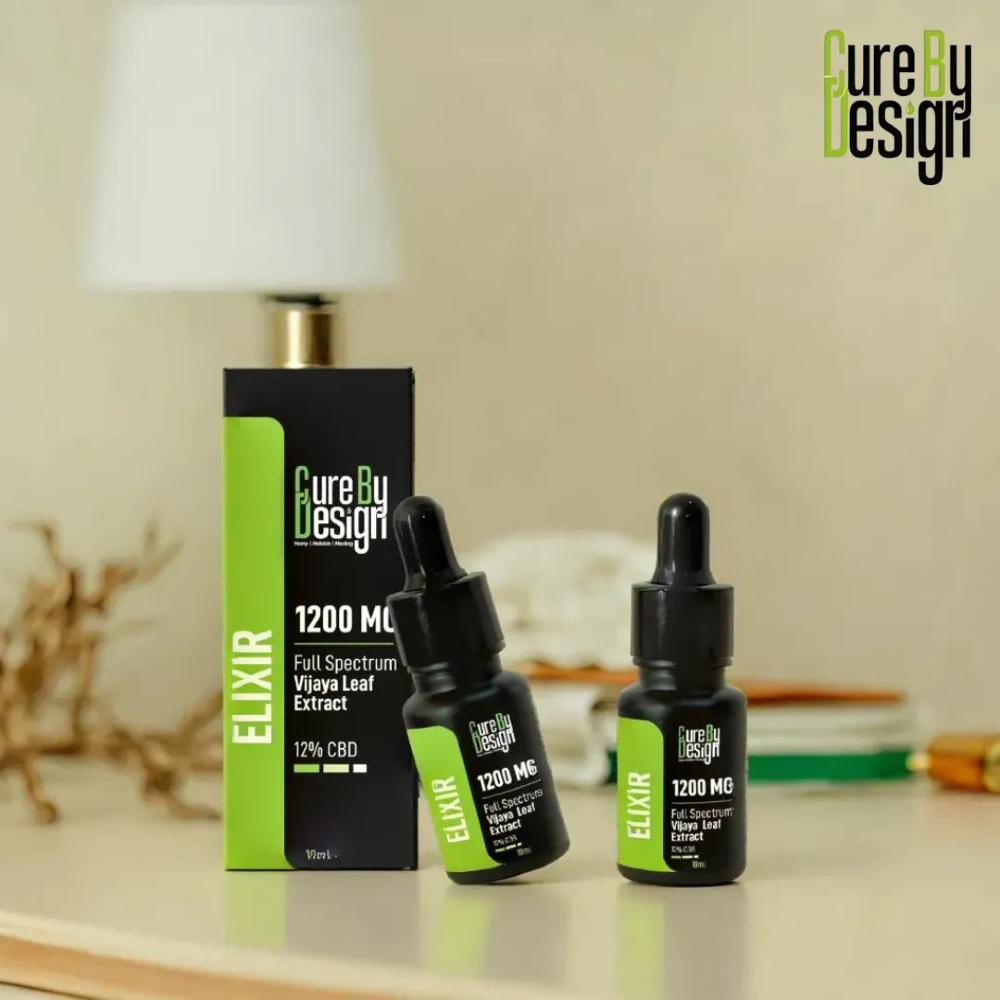 Two bottles of 'Cure By Design' elixir with a box on a table.