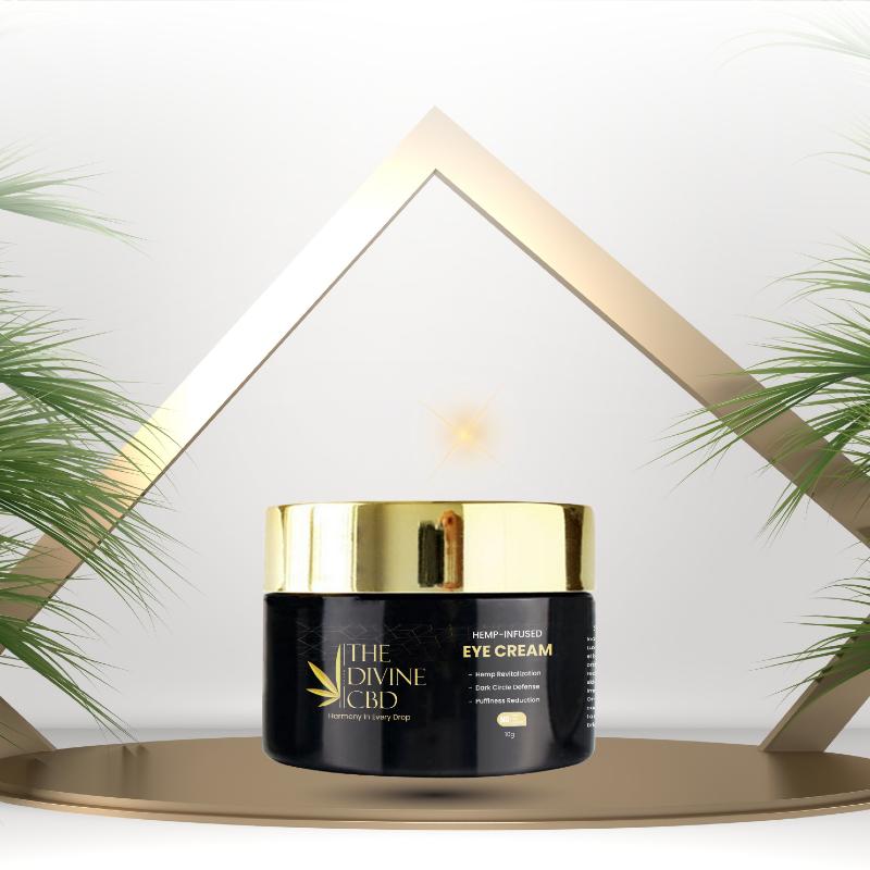 Jar of "The Divine CBD Hemp-Infused Eye Cream" on a platform with a gold triangular frame and palm leaves in the background.
