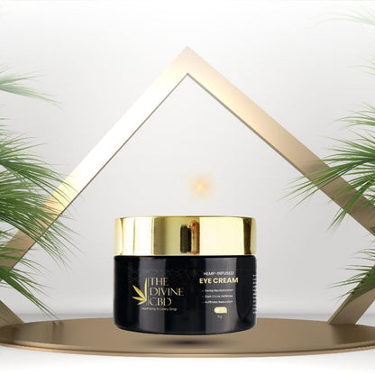 Jar of "The Divine CBD Hemp-Infused Eye Cream" on a platform with a gold triangular frame and palm leaves in the background.