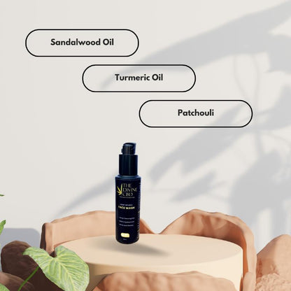 Black bottle labeled "THE DIVINE CBD FACE WASH" on beige pedestal surrounded by rocks, with labels.

