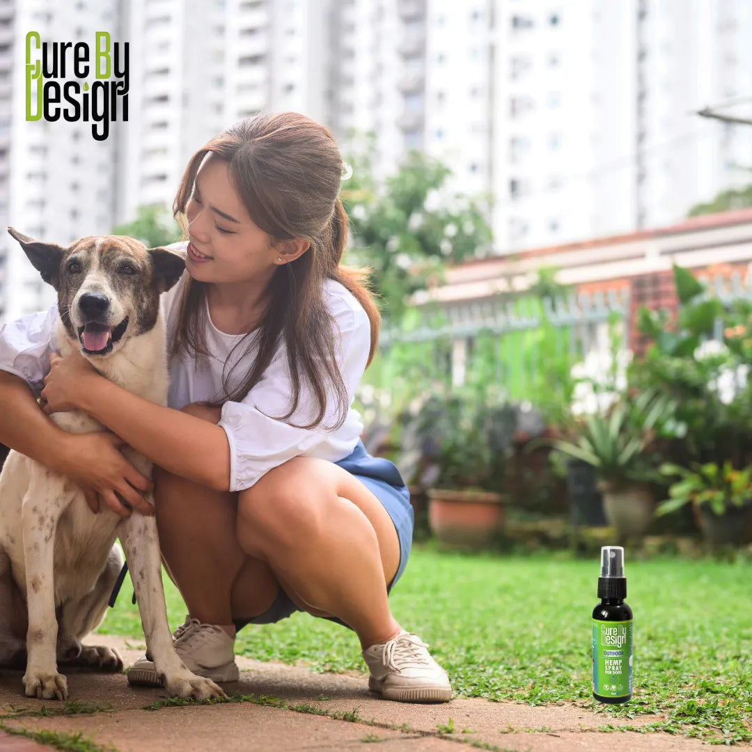 Woman holding a dog with a bottle of 'Cure by Design Hemp Spray' product on grass