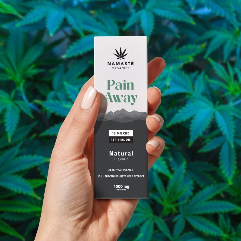 Hand holding a Namaste Organics Pain Away Full spectrum CBD Oil  supplement packet against a green leafy background