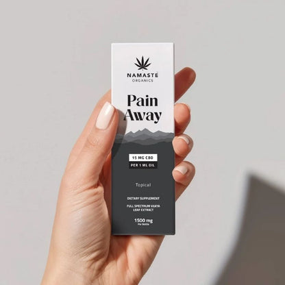 Hand holding a 'Pain Away' Full spectrum CBD Oil product box by Namaste Organics against a gray background