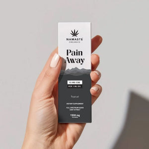 Hand holding a 'Pain Away' Full spectrum CBD Oil product box by Namaste Organics against a gray background