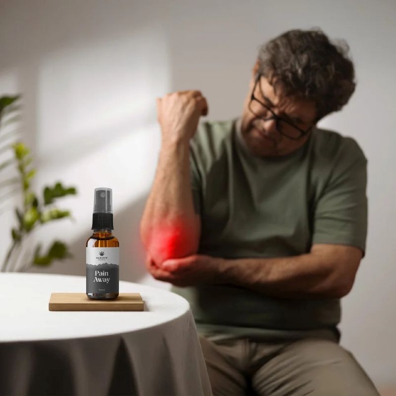 Man with a painful arm holding a bottle labeled 'Pain Away -  Full spectrum CBD Oil' on a table.