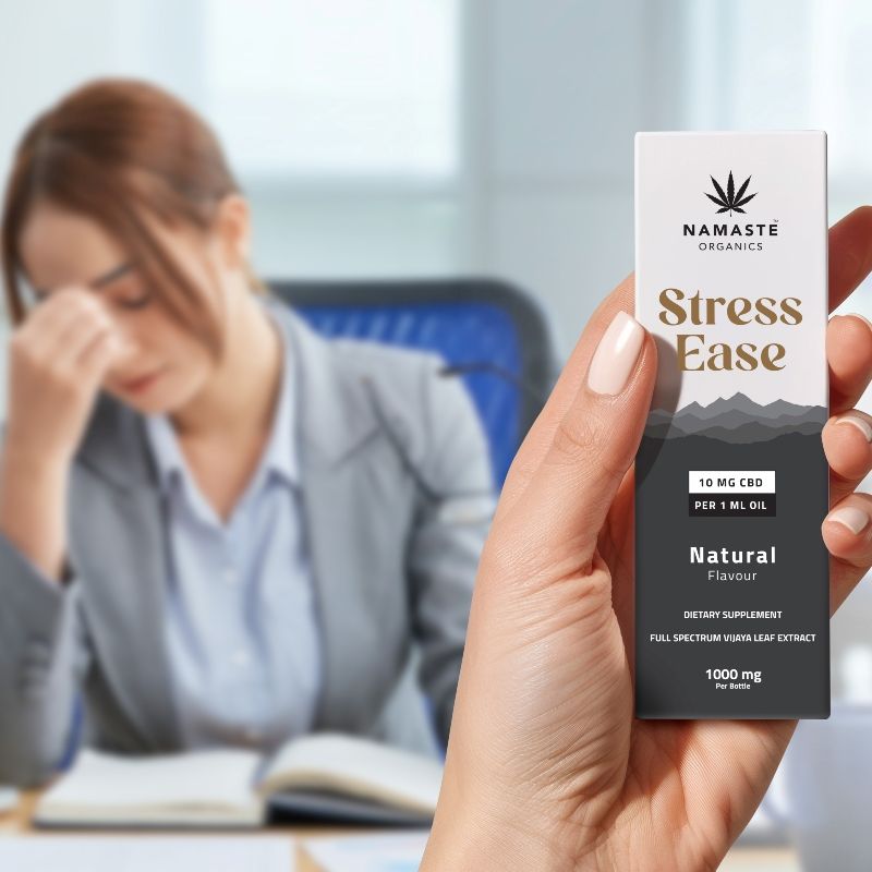 Hand holding a 'Namaste Organics Stress Ease' Full spectrum CBD Oil product with a blurred background of a person working.