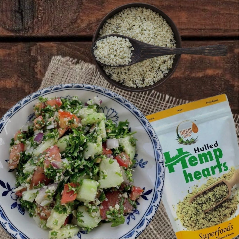 Hulled hemp hearts on a wooden surface with a salad and packaging.