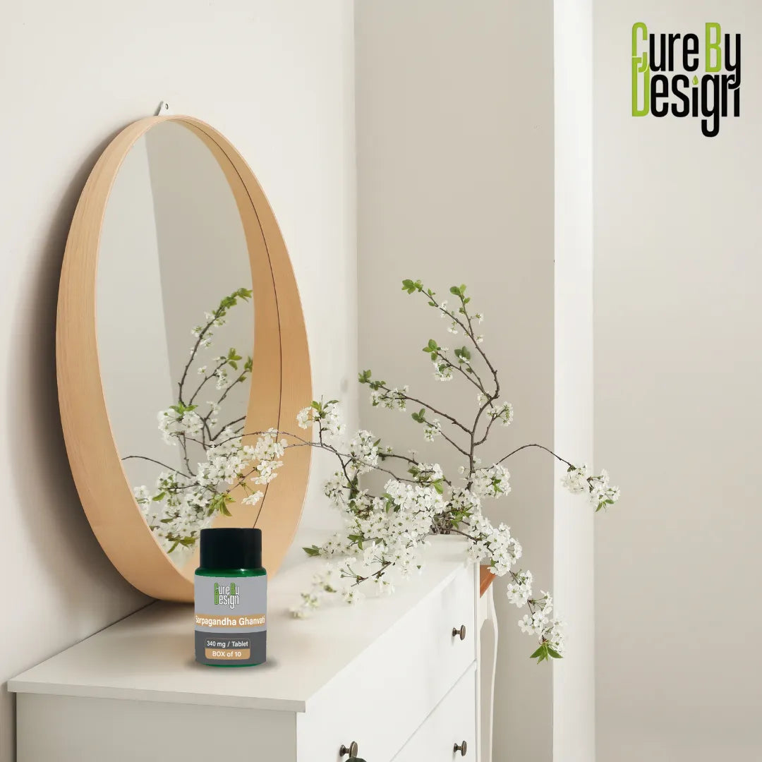 Round mirror on a shelf with white flowers and a bottle labeled 'Cure by Design' against a light gray wall.