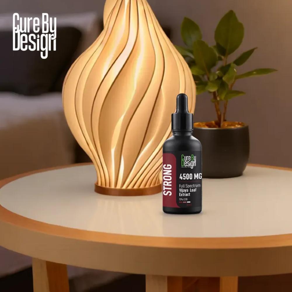 Cure By Design CBD Oil bottle on a table with a lamp and plant in the background