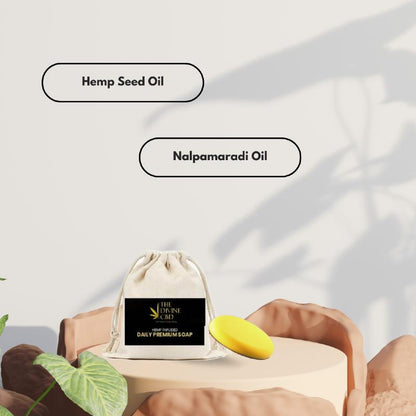 Drawstring bag labeled “THE DIVINE CBD. HEMP INFUSED DAILY PREMIUM SOAP” with yellow soap on a podium. Labels read “Hemp Seed Oil” and “Nalpamaradi Oil.”