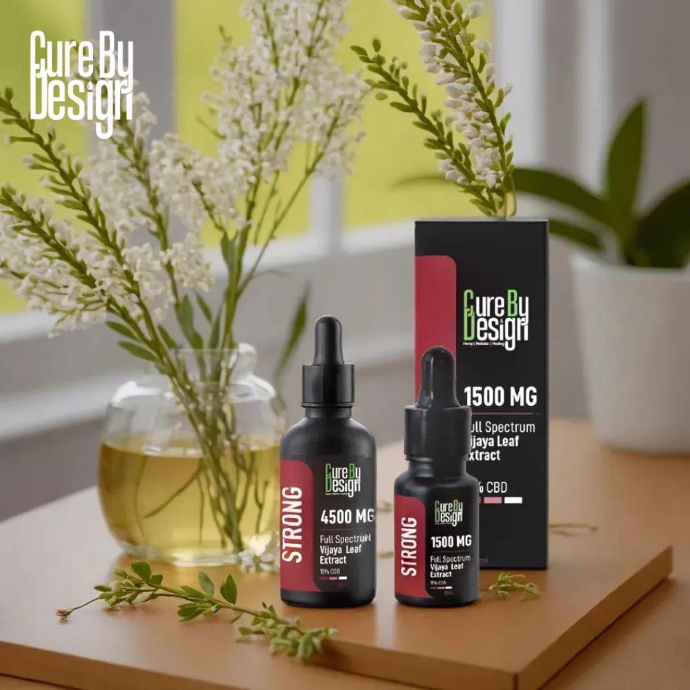 Two bottles of Cure By Design CBD products on a wooden surface with flowers and packaging in the background.