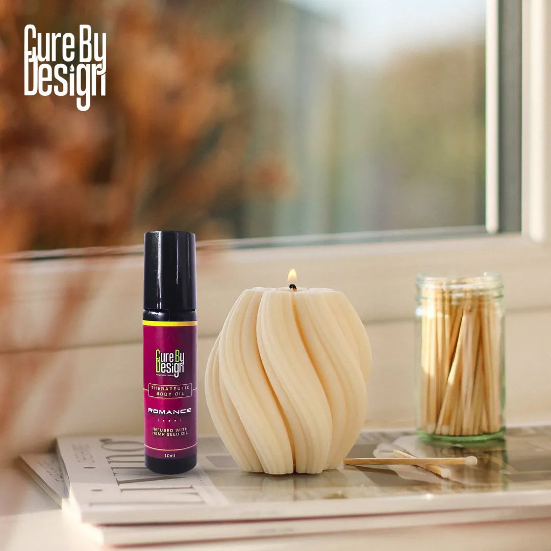 Candle and bottle with 'Cure By Design' branding on a surface.