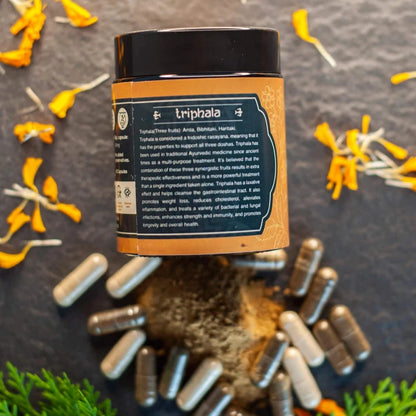  A container of Triphala with scattered yellow flower petals and capsules around it.

