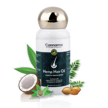 Load image into Gallery viewer, Bottle of hemp hair oil with a gold cap on a wooden surface, flanked by green leaves against a light background.
