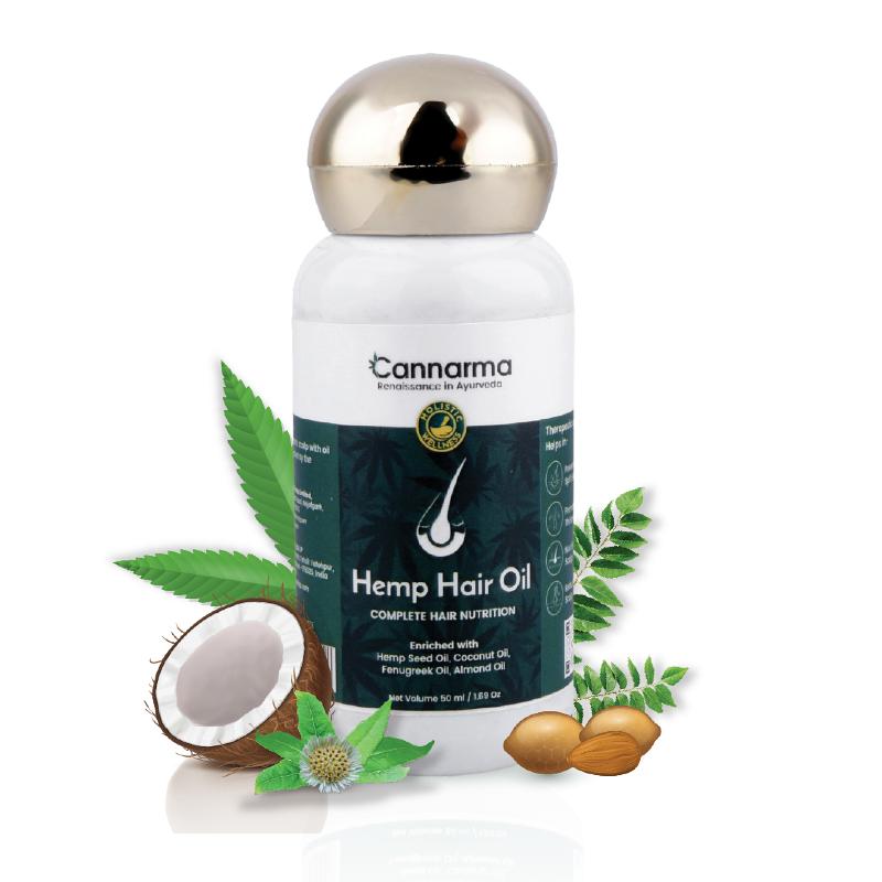 Bottle of hemp hair oil with a gold cap on a wooden surface, flanked by green leaves against a light background.