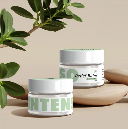 Two jars of awshad CBD Relief balm with green labels beside a plant, on a beige background.