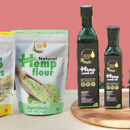 Hemp flour package and hemp seed oil bottles on a wooden board with a pink background