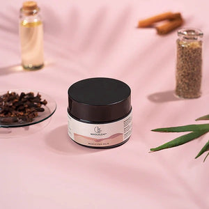 Jar of muscle pain balm on a pink background with cinnamon sticks and herbs.