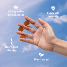 Load image into Gallery viewer, A hand holding four square shaped cannabis gummies against a blue sky with text: &quot;40 mg active cannabinoids, Extra safe formula, Retro cola flavour, Plant-based.&quot;
